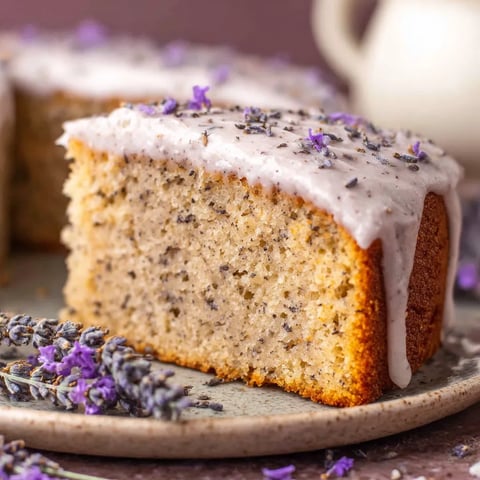 A slice of London Fog cake with white frosting and purple flowers.