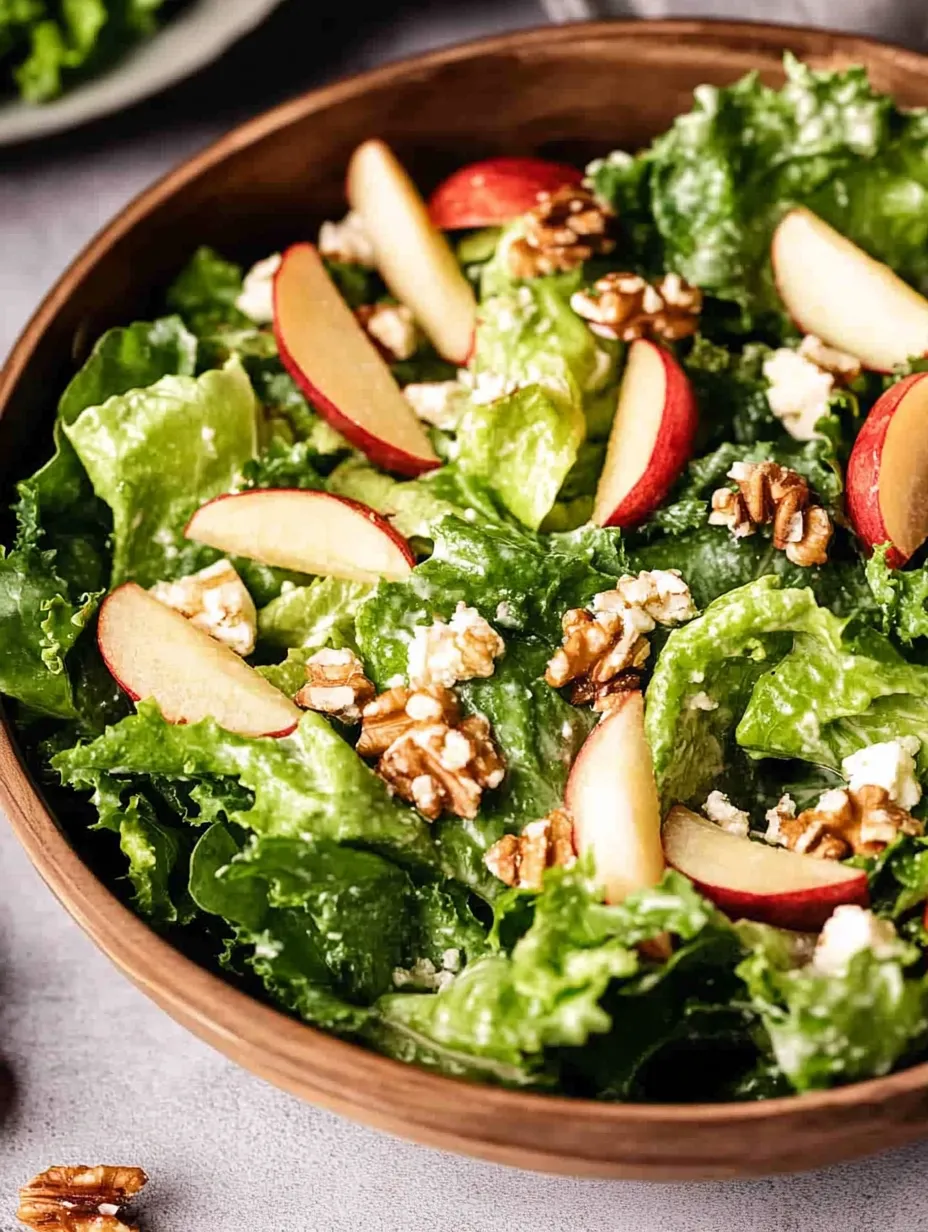 A bowl of salad with apples, walnuts, and lettuce.