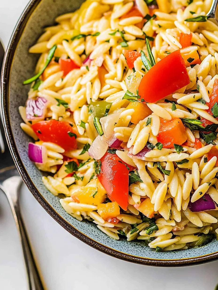A bowl of pasta salad with tomatoes, onions, and herbs.